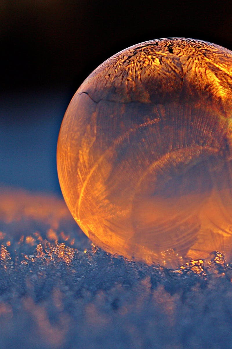 Close-up shot of a frozen bubble with warm reflections resting on a snowy surface at twilight.